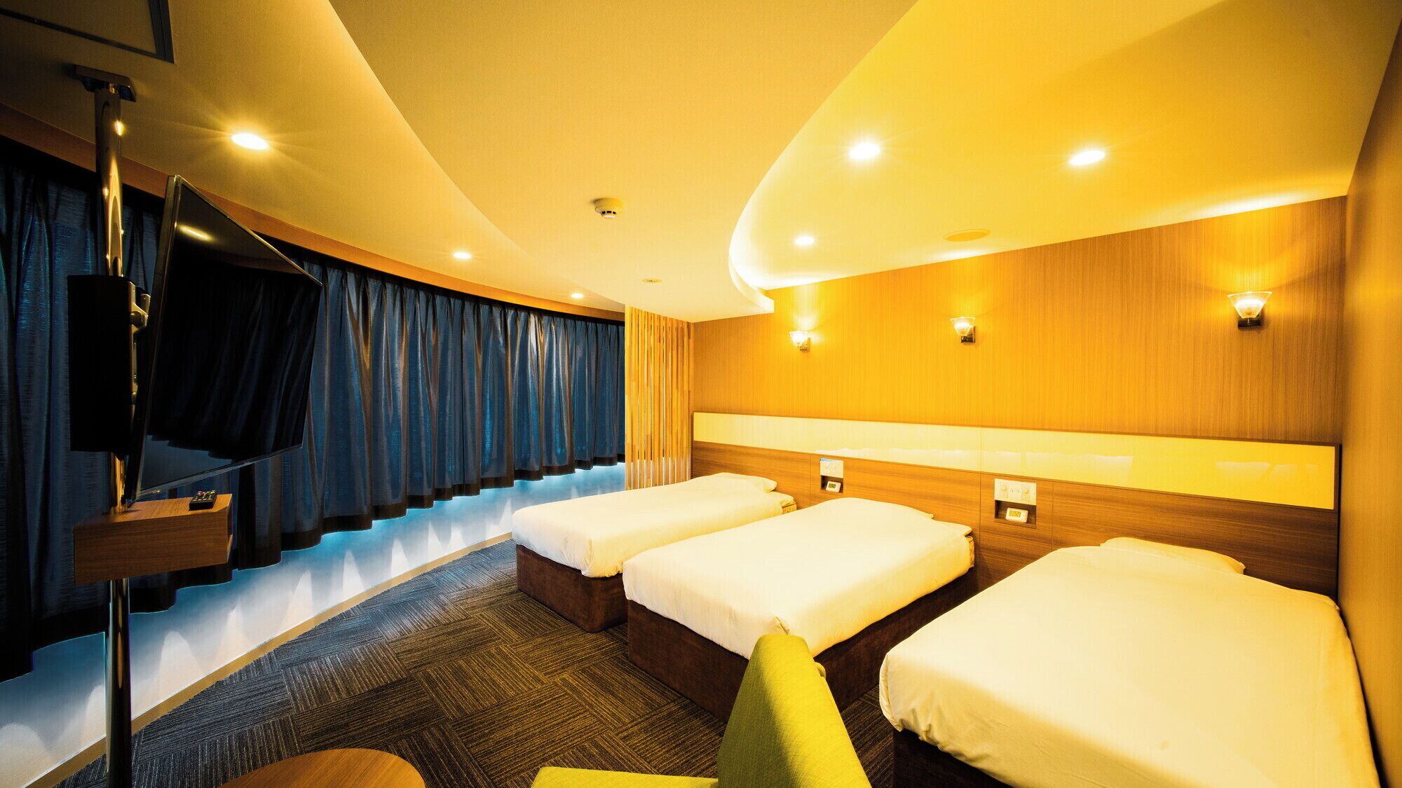 Une chambre d’hôtel avec un plafond incurvé, un téléviseur fixé au mur, un canapé et trois lits.