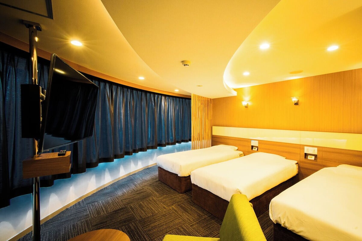 Une chambre d’hôtel avec un plafond incurvé, un téléviseur fixé au mur, un canapé et trois lits.