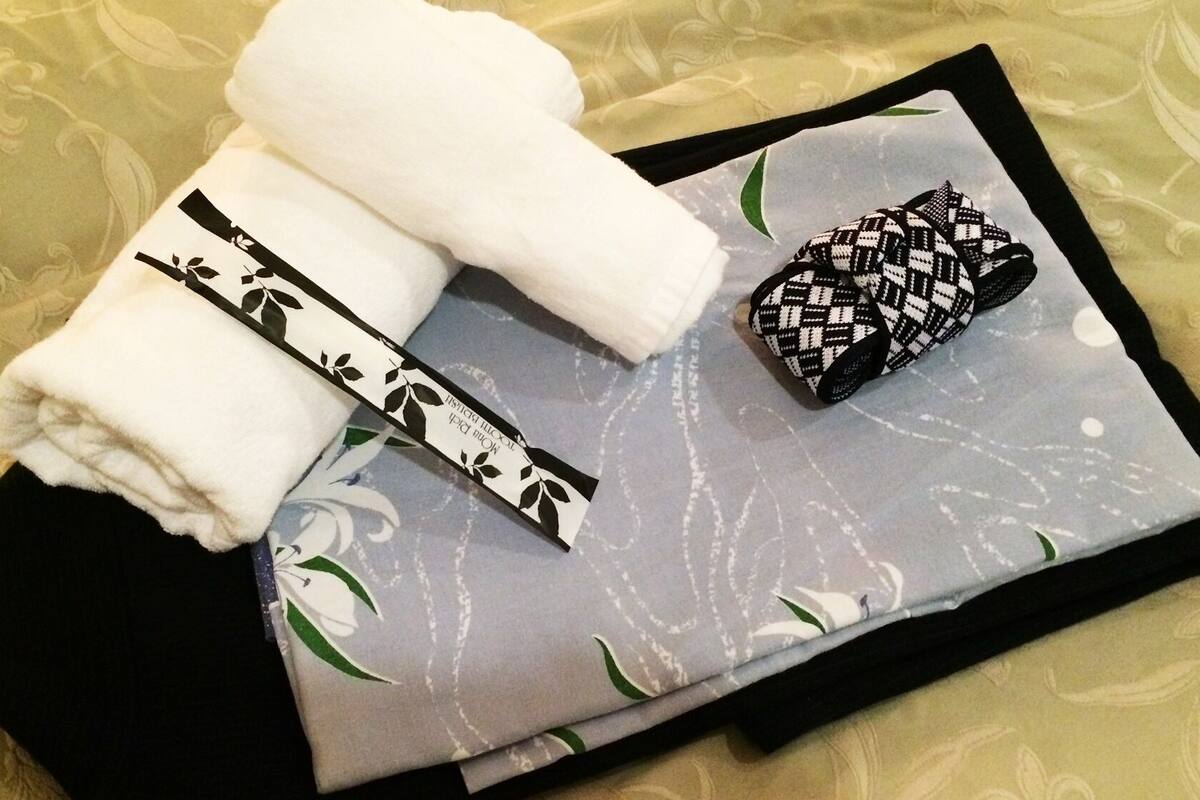 A neatly folded white towel, a black and white patterned item, and a grey pillow with floral designs on a bed with a patterned bedspread.