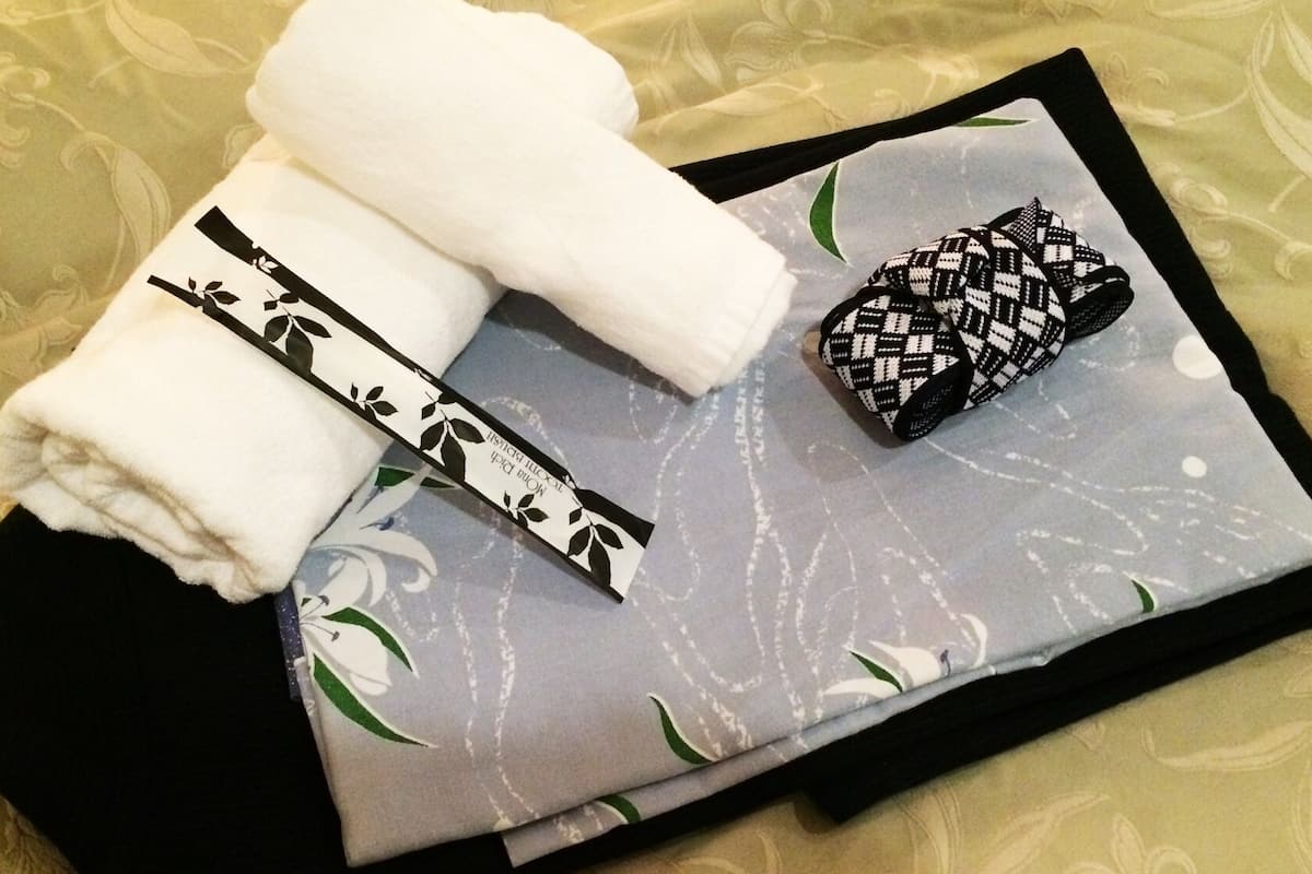 A neatly folded white towel, a black and white patterned item, and a grey pillow with floral designs on a bed with a patterned bedspread.