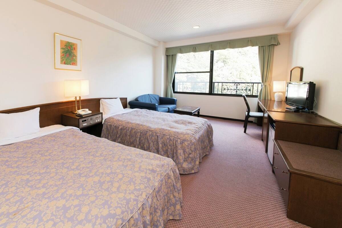 A hotel room with two beds, a desk, a chair, a television, and a window with curtains.