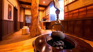 A traditional Japanese interior with a tatami mat floor, a wooden tea table with a tea kettle, and a large tree trunk. - Iyashi no Yado Iroha (Beppu)