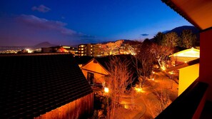Vista nocturna de un pueblo con edificios, una montaña al fondo y un sendero iluminado.