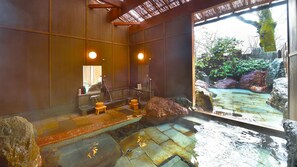A traditional Japanese onsen with a stone hot spring, wooden benches, and a view of a natural landscape through a large glass window. - Iyashi no Yado Iroha (Beppu)