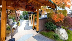 En traditionel japansk træbygning med et tag af fliser, omgivet af efterårsblade og en stensti.