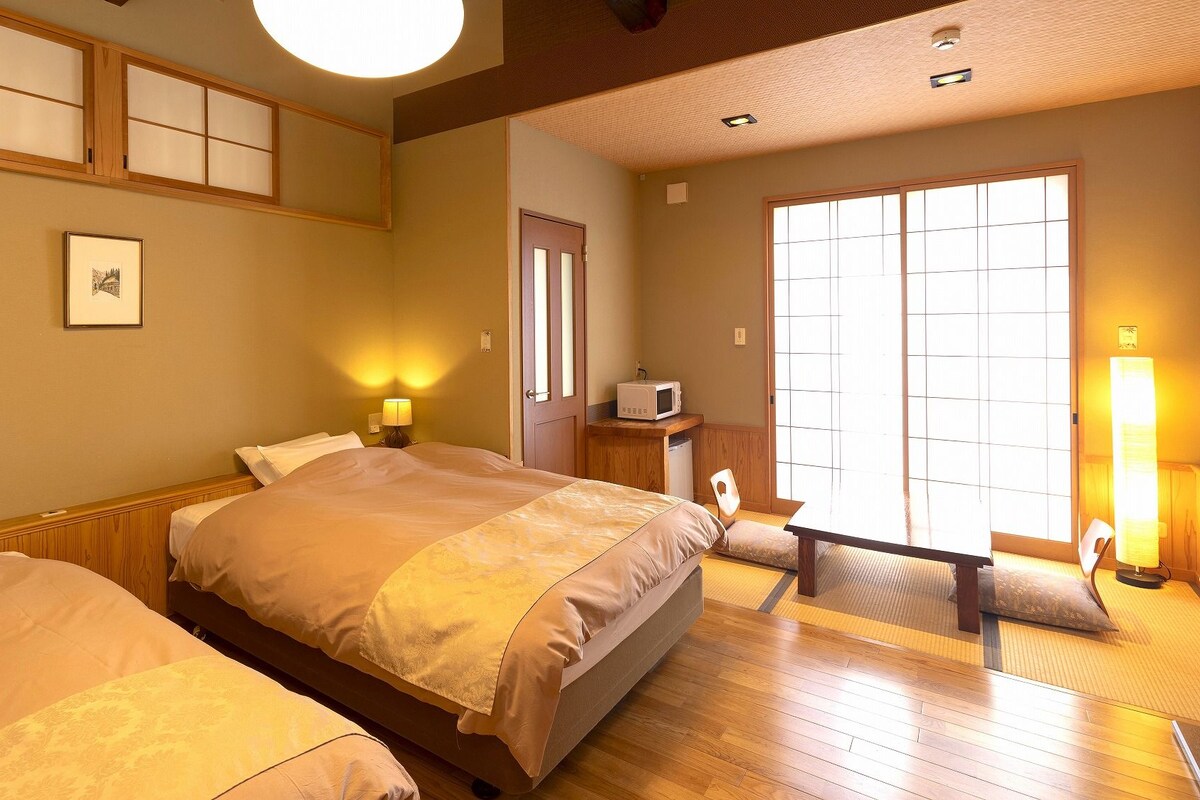 Habitación de hotel con una cama grande, lámparas de noche, microondas y puerta corrediza a un balcón.