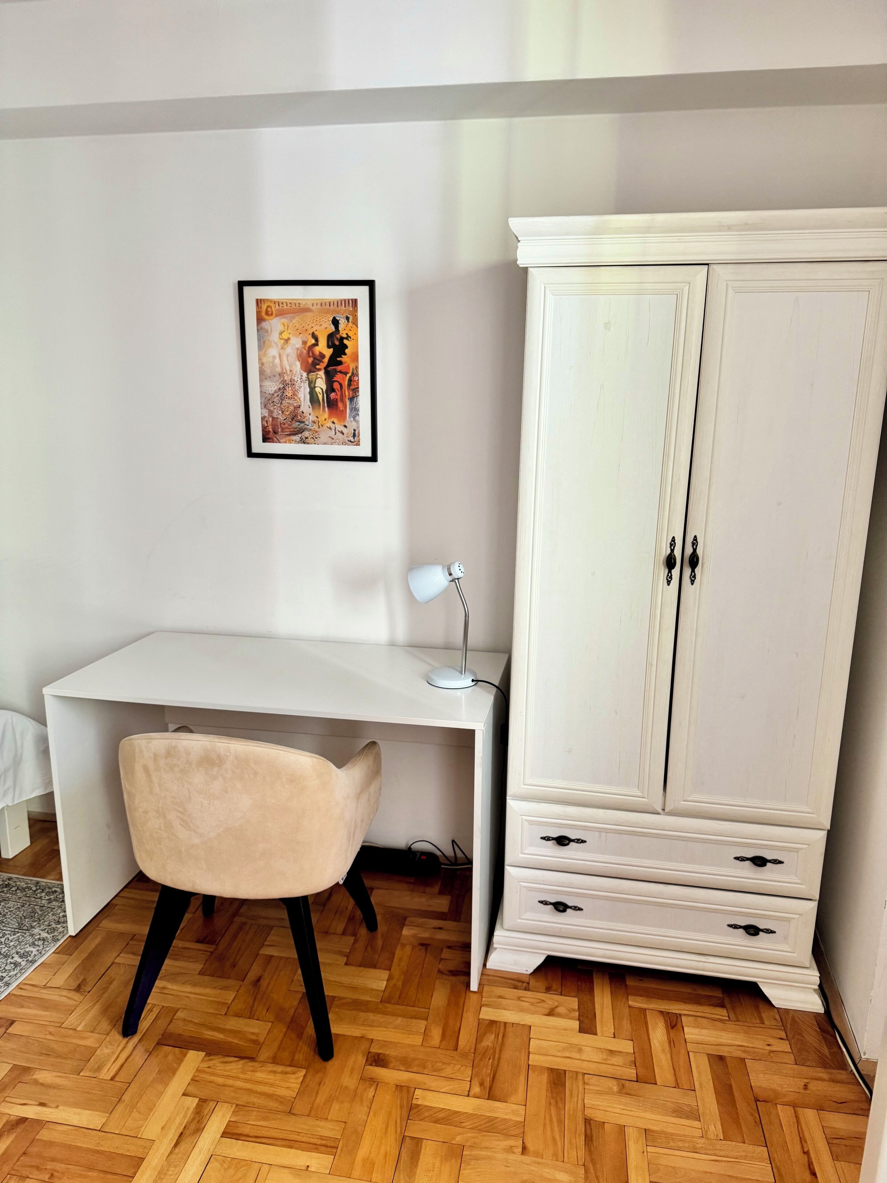 A room with a white desk, a chair, a white cabinet, and a framed picture on the wall.