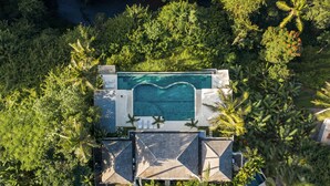 Une vue aérienne d’une piscine entourée d’une végétation luxuriante, avec une eau d’un bleu limpide et une architecture moderne.