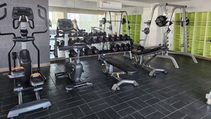 Un gimnasio con equipo de ejercicio, estantes para pesas y un muro con espejos.
