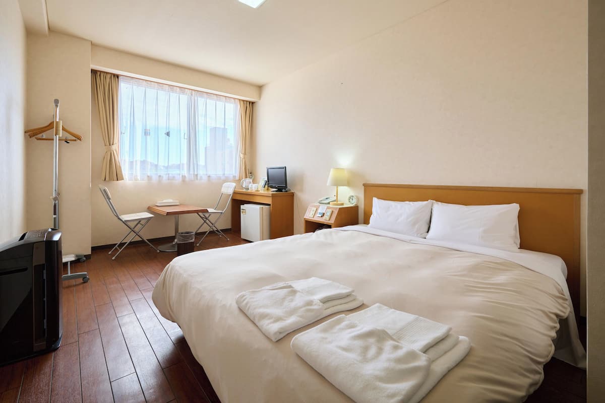 A hotel room with a large bed, a desk with a computer, a chair, and a small refrigerator.