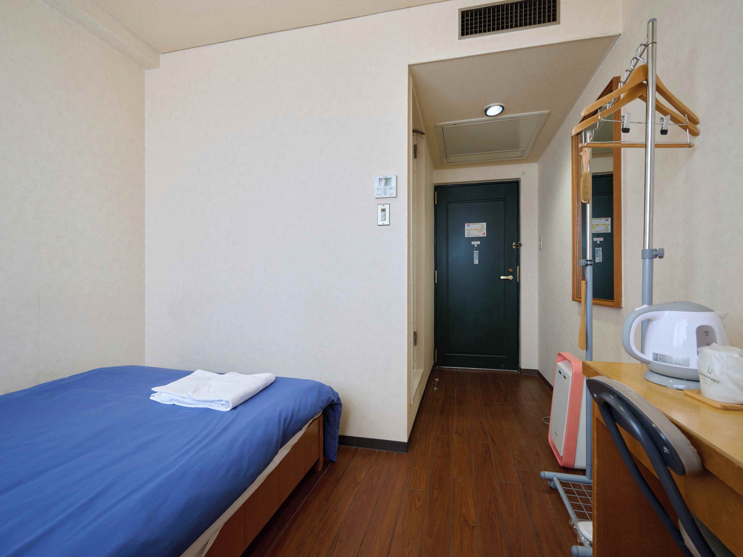 A hotel room with a single bed, a wooden desk, a mirror, a kettle, and a shower area.