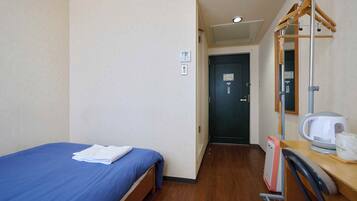 A hotel room with a single bed, a wooden desk, a mirror, a kettle, and a shower area.