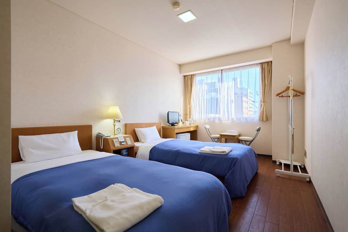 A hotel room with two beds, a desk with a computer, a chair, and a window with curtains.