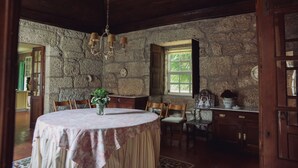 A rustic dining room with a stone wall, wooden ceiling, and a round table with a floral centerpiece. - Casa da Arosa Rural Tourism (Gandarela)