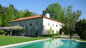 A large stone building with a red roof, surrounded by a swimming pool and lush greenery. - Casa da Arosa Rural Tourism (Gandarela)