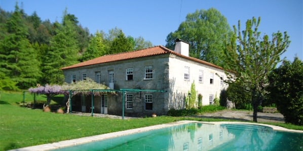 A large stone building with a red roof, surrounded by a swimming pool and lush greenery. - Casa da Arosa Rural Tourism (Gandarela)