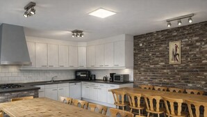 A modern kitchen with white cabinets, a wooden dining table, and a brick accent wall.