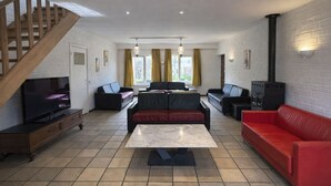 A spacious living room with a TV, sofas, a red couch, a fireplace, and a staircase.