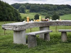 Ein rustikaler Picknicktisch in einem grasbewachsen Feld, im Hintergrund sanfte Hügel.