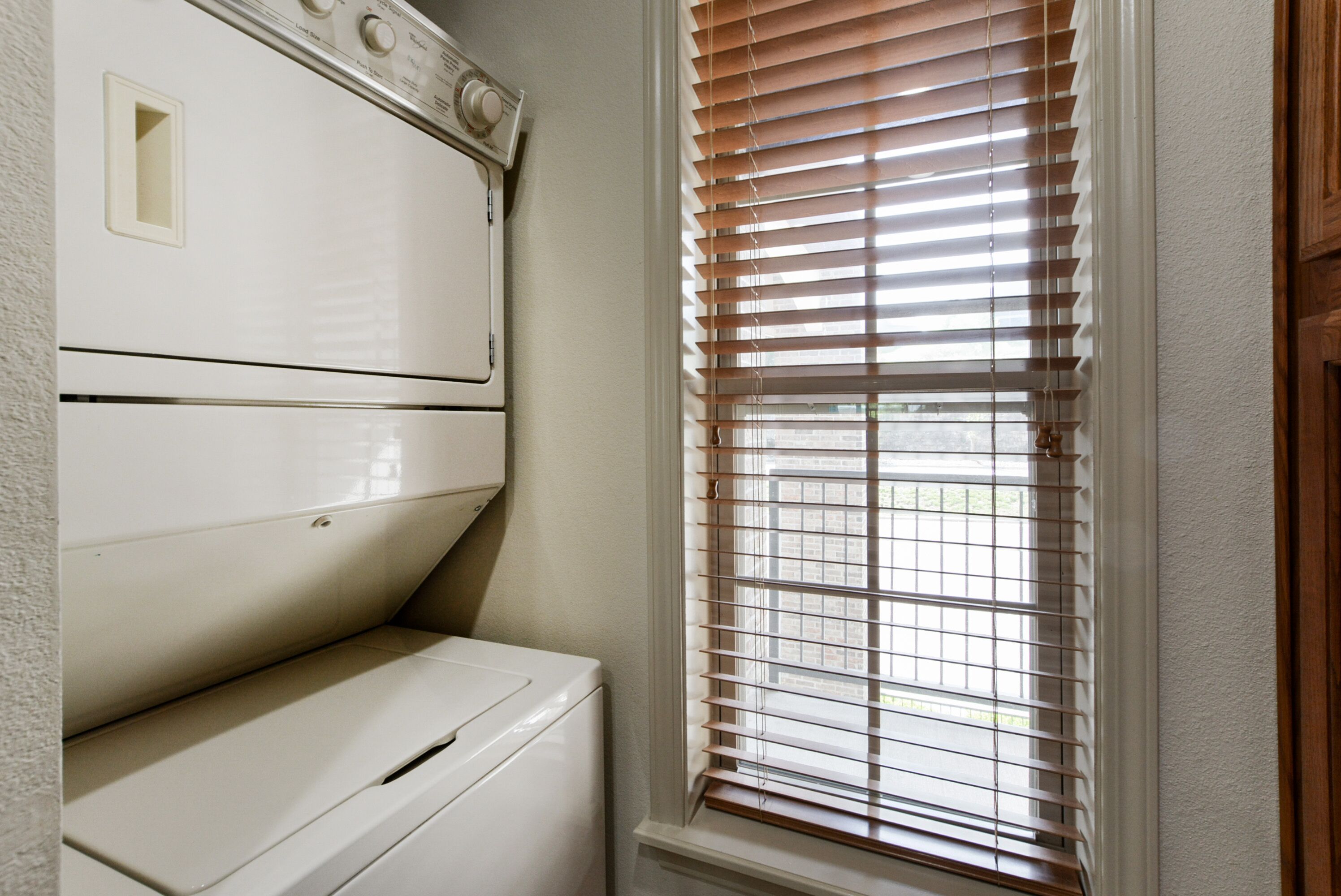 Un cuarto de lavado con lavadora y secadora blancos, una ventana con persianas y una puerta a la derecha.