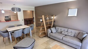 Un salon moderne avec un canapé gris, une table basse en bois et un coin repas comprenant une table blanche et des chaises grises.
