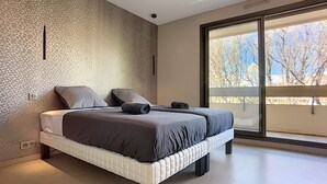 Une chambre moderne avec un grand lit, un mur orné d’un motif et une porte-fenêtre coulissante donnant sur un balcon.