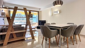 Un espace de salle à manger moderne, avec une grande table, des chaises à revêtement gris et une structure en bois originale en arrière-plan.