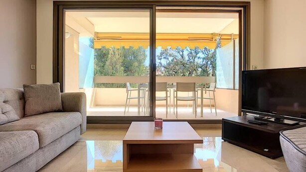 Un salon moderne avec un canapé, une table basse, un téléviseur et un balcon aménagé avec du mobilier d’extérieur.