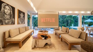 Uma sala de estar moderna com uma tela grande exibindo 'NETFLIX', um sofá, uma mesa de centro e vista para o exterior.
