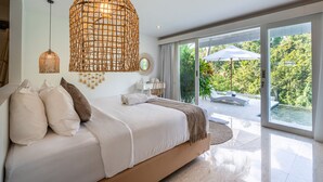 Quarto com cama grande, luminária pendente e vista para uma piscina e vegetação lá fora.