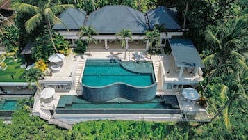 A large, modern house with a swimming pool, surrounded by lush greenery and palm trees.