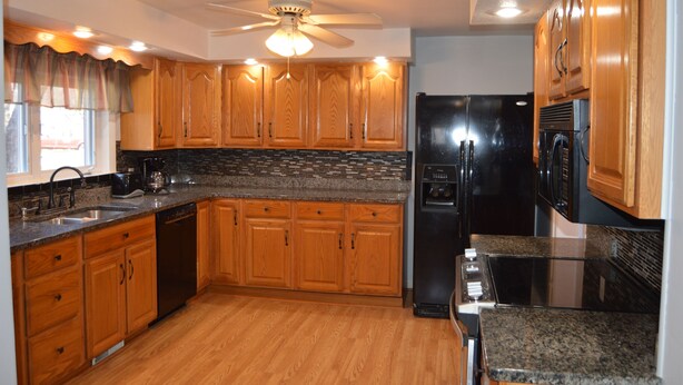 A kitchen with wooden cabinets, a black refrigerator, a microwave, and a dishwasher. - 4 Bedroom Home Near Warren Dunes State Park (Sawyer)