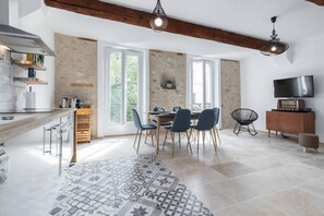 A modern kitchen with a wooden countertop, a dining area with a table and chairs, and a stone wall. - (13c) Le marche Provencal (Antibes)