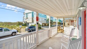 A covered porch with white railings, outdoor seating, and a view of buildings and vehicles. - Vitamin Sea Suites 4: Downtown and a short walk to the SEA! (Carolina Beach)