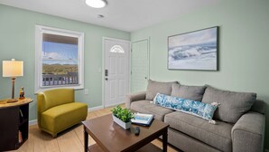 A living room with a sofa, a coffee table with a plant, a lamp, and a door with a window. - Vitamin Sea Suites 4: Downtown and a short walk to the SEA! (Carolina Beach)