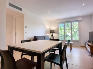 Uma sala de estar moderna com área de jantar, sofá, luminária e TV.