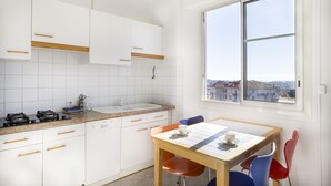 A kitchen with white cabinets, a wooden countertop, a sink, and a window with a view of buildings. - Bright, 63m², panoramic view of city and sea. Garage (Cannes)