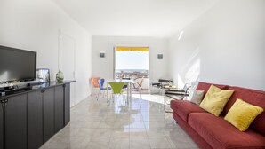 A modern living room with a red sofa, a TV, and a dining area with colorful chairs. - Bright, 63m², panoramic view of city and sea. Garage (Cannes)