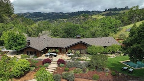 A modern house with a large front yard, a swimming pool, and a view of rolling hills.