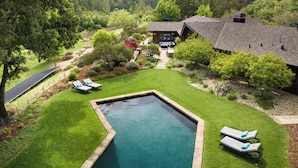 A swimming pool with two lounge chairs and a well-maintained lawn, surrounded by trees and a house.