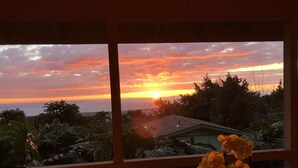 A sunset view through a window with tropical foliage and a house in the background. - New Listing: Spacious Suite for 4x with panoramic ocean view (Kailua)
