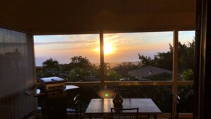 A dining area with a table and chairs, a grill, and a view of the sunset through large windows. - New Listing: Spacious Suite for 4x with panoramic ocean view (Kailua)