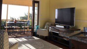 A living room with a ceiling fan, a flat-screen TV, a dining area with a table and chairs, and a large window. - New Listing: Spacious Suite for 4x with panoramic ocean view (Kailua)