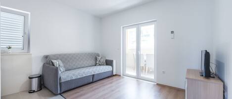 A modern living room with a grey sofa, a small cabinet, and a television.