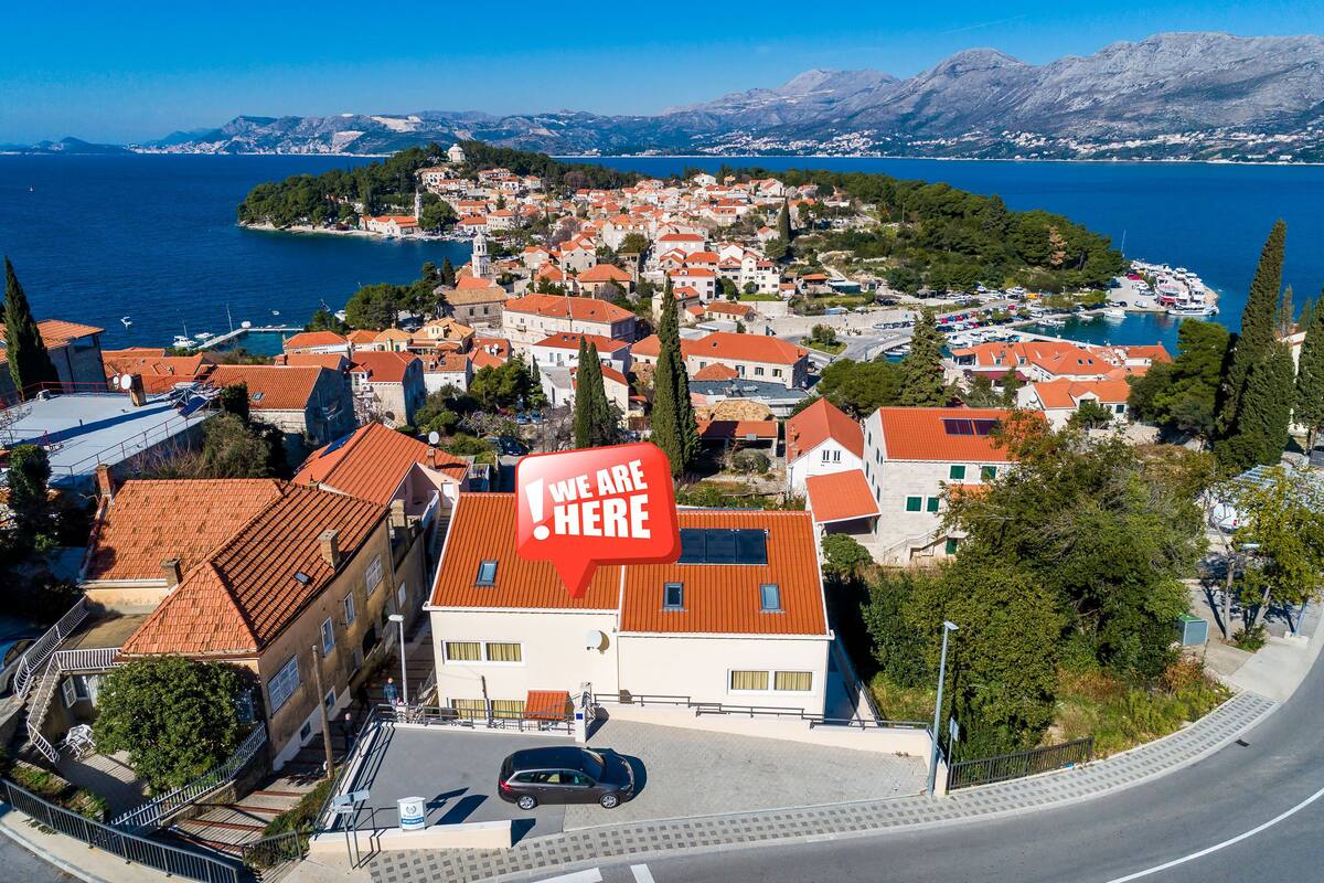 Une ville côtière aux bâtiments aux toits rouges, dotée d’un port de plaisance et offrant une vue dégagée sur la mer et les montagnes en arrière-plan.