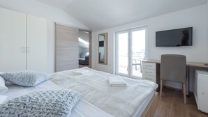 Ein modernes Schlafzimmer mit einem großen Bett, einem Schreibtisch, einem Fernseher und Blick auf einen Balkon.