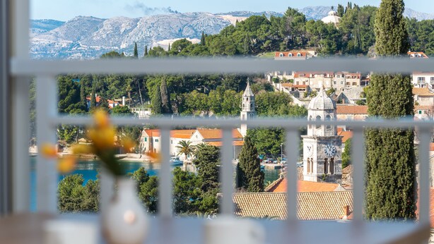 Blick aus einem Fenster auf eine Stadt mit historischen Gebäuden, einem Glockenturm und Bergen im Hintergrund.