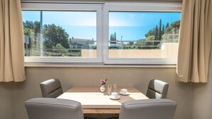 Ein Essbereich mit Tisch und Stühlen, einer Vase mit Blumen sowie Blick auf das Meer und Bäume durch große Fenster.