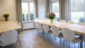 Un vaste espace dédié à la salle à manger, avec une longue table en bois, des chaises blanches et de grandes fenêtres dotées de rideaux.