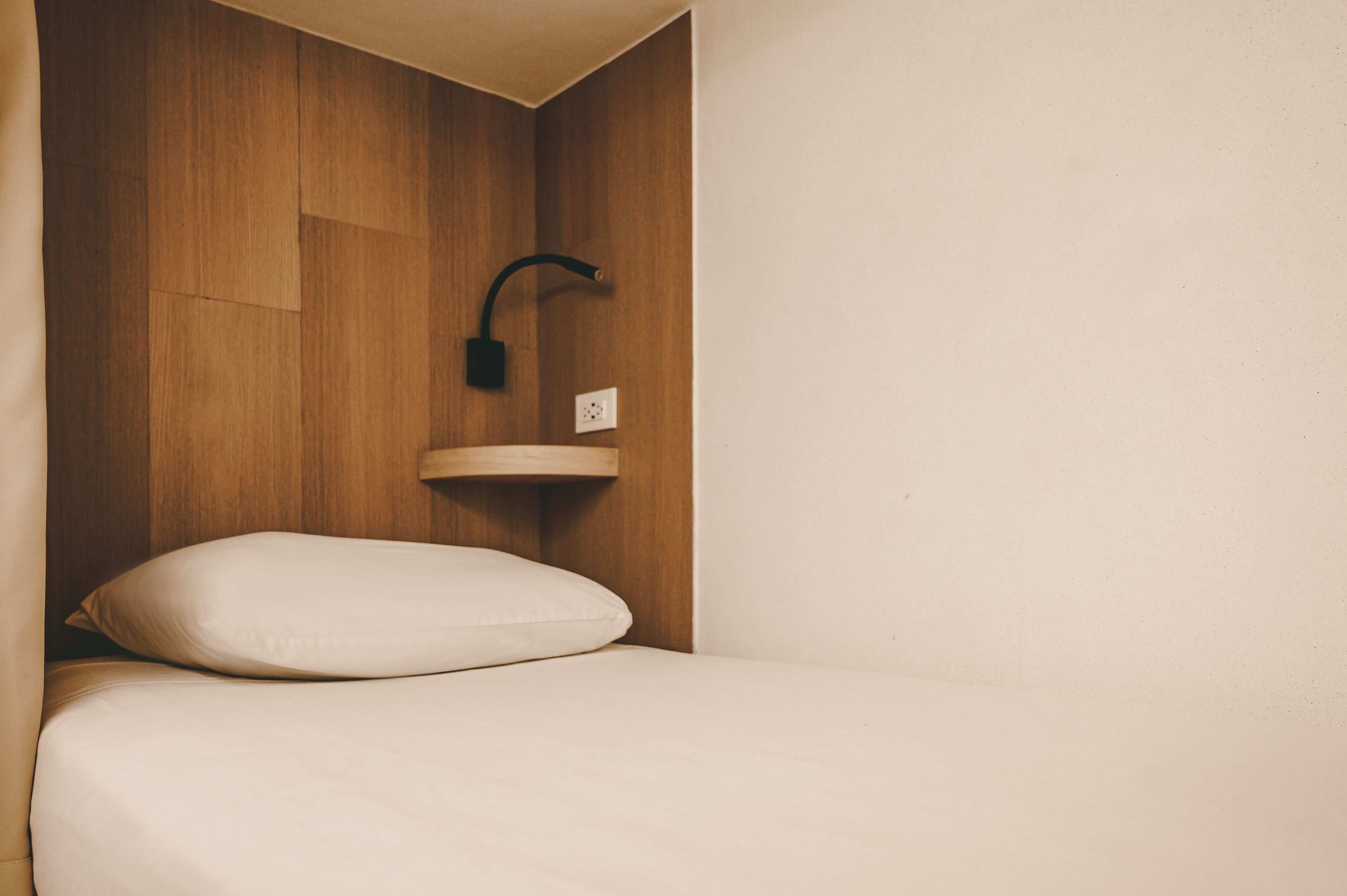 A small, neatly made bed with a single white pillow and a wooden headboard.